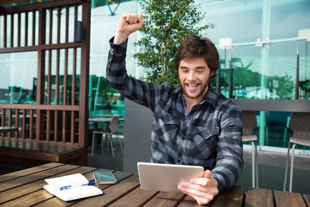 happy man using tablet and celebrating achievement in cafe